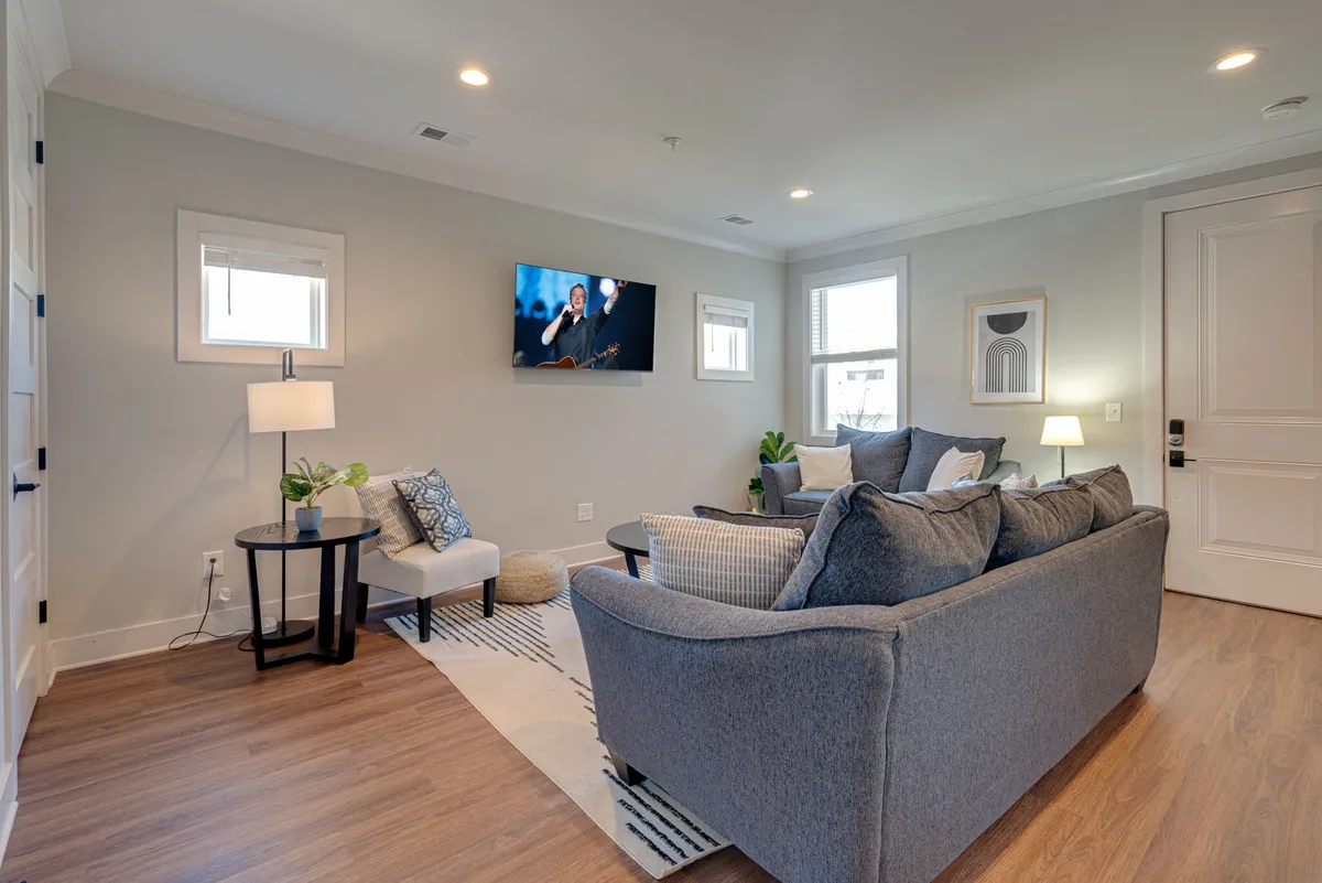 The image showcases a welcoming and stylish living room with a plush sofa, a large television, warm lighting from a lamp, and touches of greenery from a plant. The space exudes comfort, inviting guests to relax, watch TV, and gather for memorable group experiences.