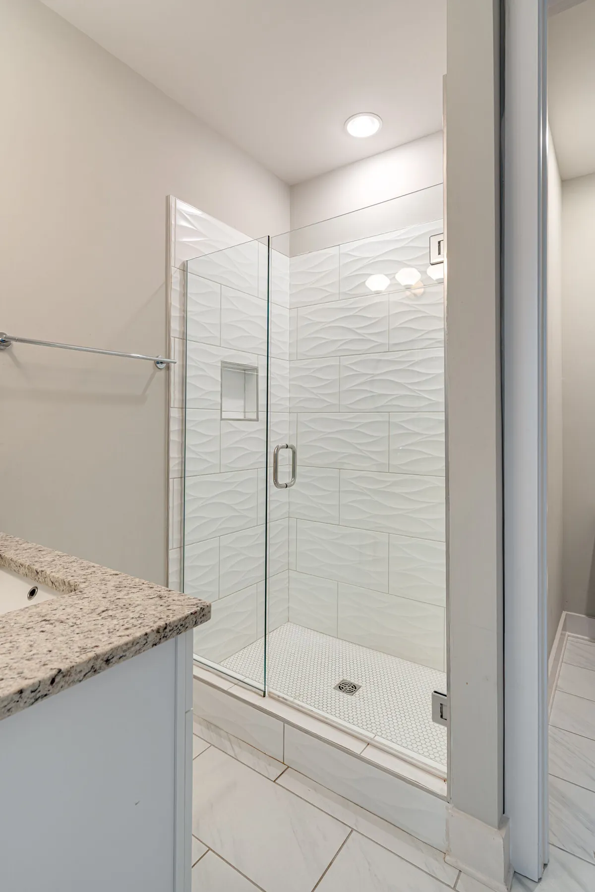 A modern bathroom with a glass shower enclosure, granite countertop, and textured wall tiles. The space is clean, bright, and tranquil—ideal for refreshing after a long day.