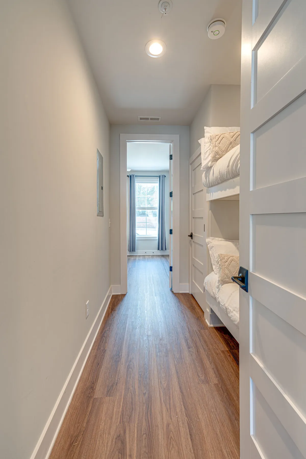 This image features a cozy interior with bunk beds, a doorway leading to a bright adjoining room, and hardwood floors. The design and layout suggest a welcoming and family-friendly entry area, reinforcing the idea of shared spaces and group comfort.