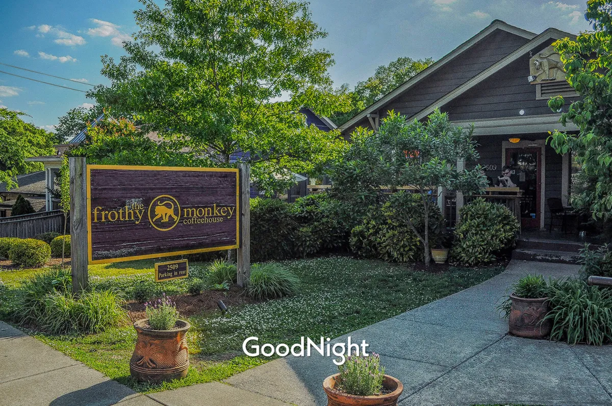 The exterior view of the Frothy Monkey coffeehouse, showcasing its signage, landscaped garden, and welcoming entrance. The setting includes outdoor seating, inviting customers to enjoy coffee or work in a relaxed, social atmosphere.