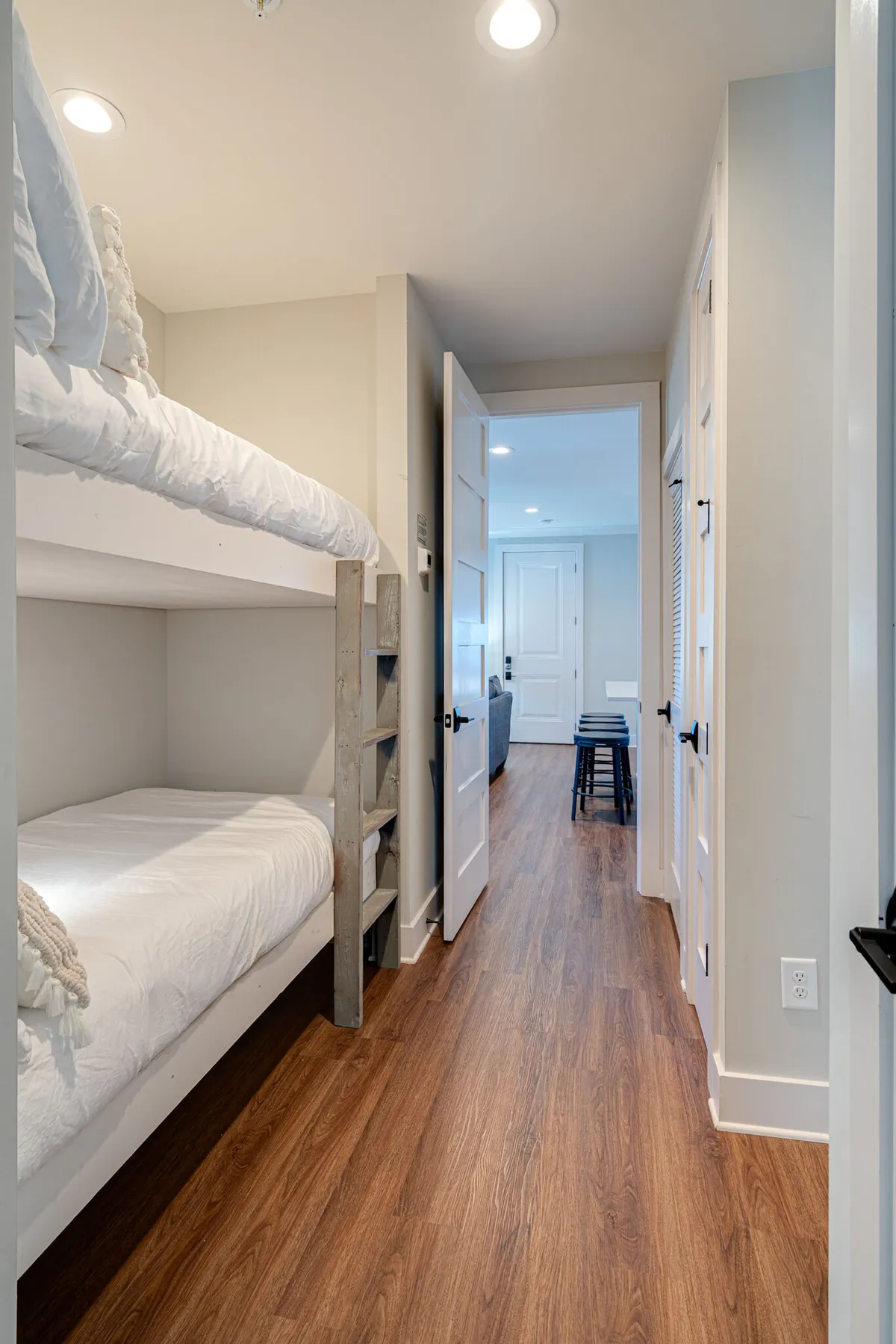 A set of built-in bunk beds with wooden flooring and a door leading to an adjacent room. The beds are arranged to create a cozy nook, ideal for children or extra guests. The space is designed to be functional and inviting, supporting group or family stays.